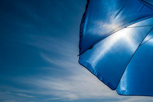 Vibrant blue beach umbrella against sun and clear sky