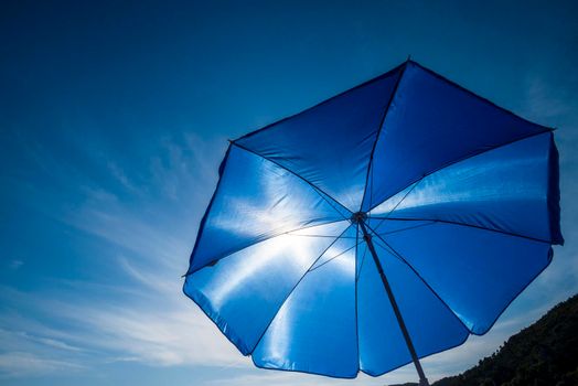Vibrant blue beach umbrella against sun and clear sky