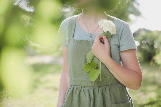young woman in apron holding flowers in the garden in summer. gardening and profession concept