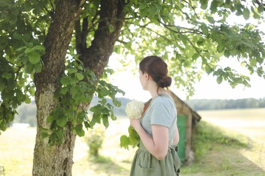 young woman in apron holding flowers in the garden in summer. gardening and profession concept