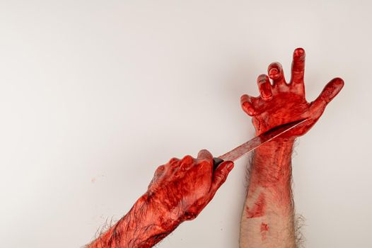 A man with bloody hands cuts himself with a knife