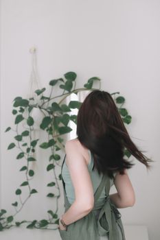 Young woman in apron as housewife or gardener takes care of green plant, watering flower pots in cozy room. gardening and hobby