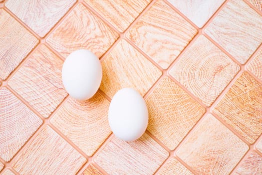 an oval or round object laid by a female bird, reptile, fish, or invertebrate, usually containing a developing embryo. Three chicken bird eggs on a wooden pink orange checkered surface.