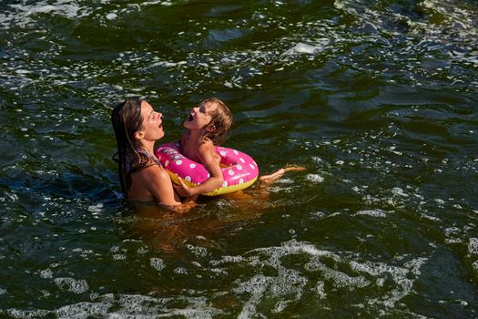 propel the body through water by using the limbs,by using fins, tail, or other bodily movement.Cute girl on a swimming circle bathes with her mother protecting her in the sea.