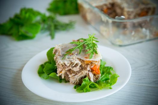 jellied meat with greens and vegetables in a plate on a wooden table