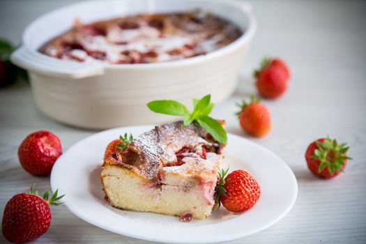 Sweet cottage cheese casserole with strawberry filling, in a plate on a wooden table.