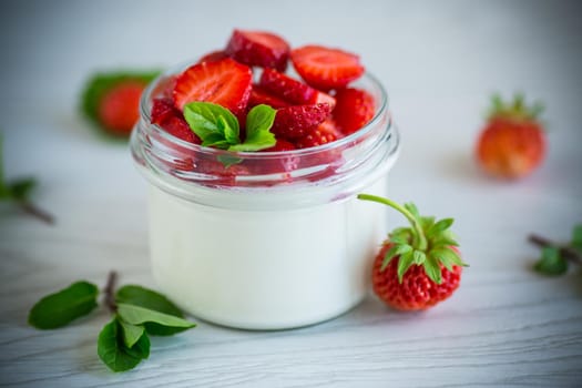 Sweet homemade yogurt with fresh ripe strawberries in a glass jar on a light wooden table