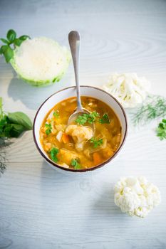 vegetable summer soup with cauliflower in a bowl on a light wooden table