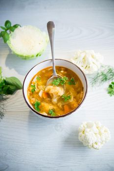 vegetable summer soup with cauliflower in a bowl on a light wooden table