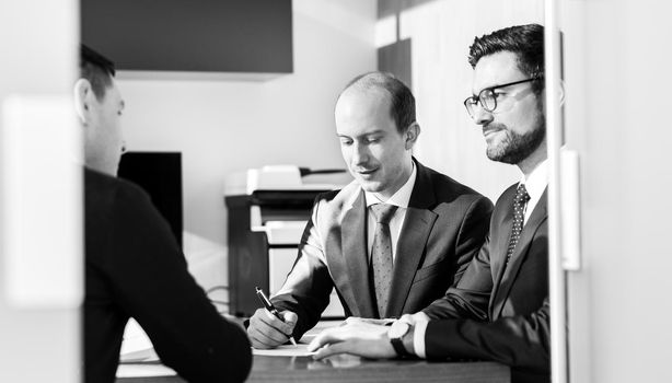 Team of confident successful business people reviewing and signing a contract to seal the deal at business meeting in modern corporate office. Business concept. Black and white image.