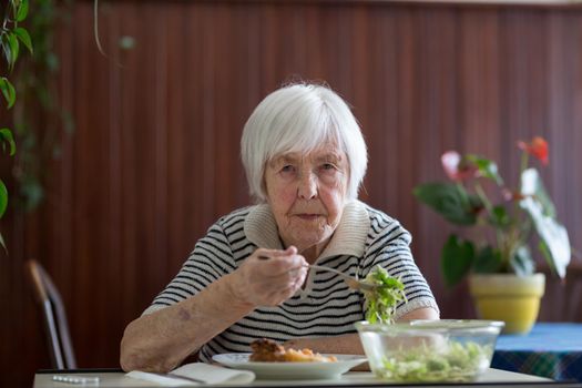 Lonley solitary elderly woman having lunch alone sitting at the table at home. Lonely late life period of a widow