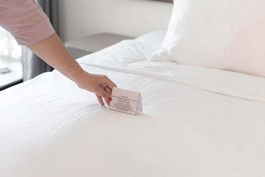Woman hands putting signboard change bed sheets on the bed