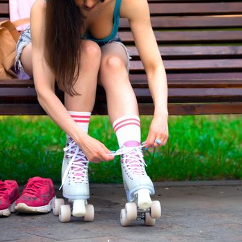 Female skater binds the roller skates on the bench in a park