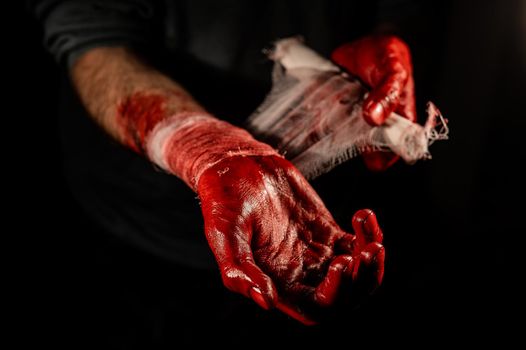 A man covered in blood bandages his hands