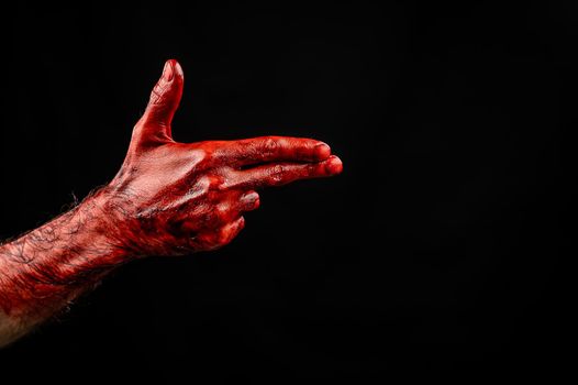 Bloody male hand gesturing shows a gun against black background