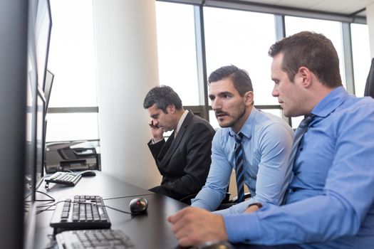 Worried business team brainstorming in corporate office. Stock traders looking at graphs, indexes and numbers on multiple computer screens in time of bear stock market. Crisis management.