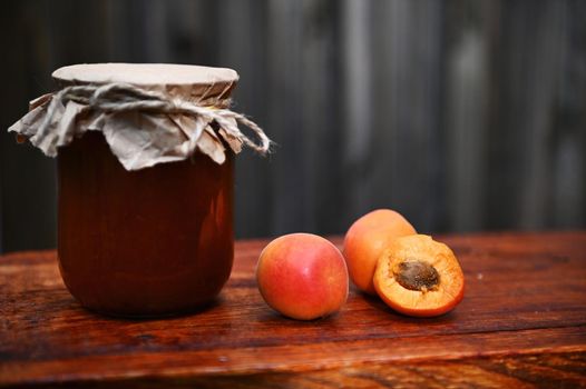 Still life. Close-up of a jar of homemade apricot confiture and ripe ready-to-eat apricots on a rustic wooden surface. Canning concept. Copy ad space for text