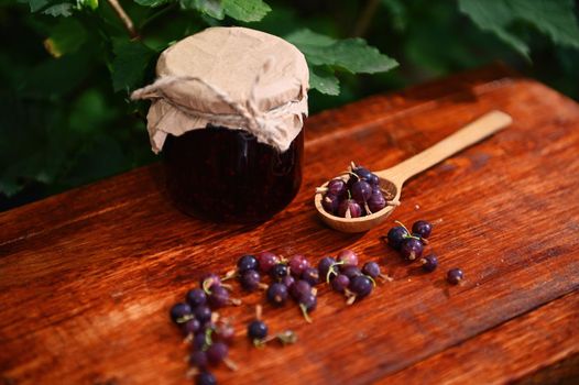 Still life. View from above of a jar of a homemade wild berry confiture, wooden spoon and gooseberries on a rustic wood surface. Canning concept. Sweet healthy food. Organic farm, culinary traditions