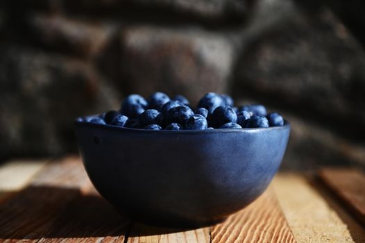 Still life. Close-up composition on a blue ceramic bowl of fresh navy wild blueberries from an organic farm on a rustic wooden crate and gray stone background. Copy space for advertising text. Banner