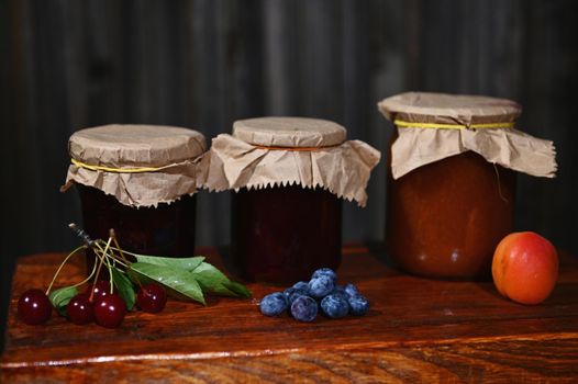 Collection of jars with homemade jam, confiture and jelly with fresh ripe seasonal fruits and berries on a rustic wooden surface. Canning, preparation of preserved food for winter season. Still life