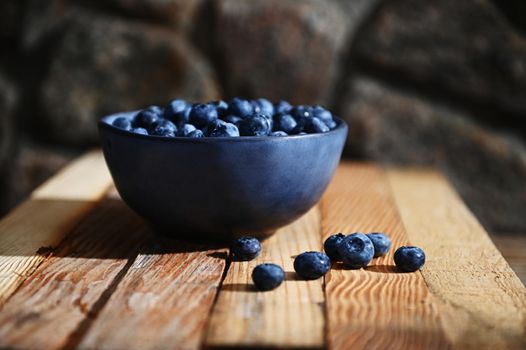 Food composition of a blue ceramic bowl of fresh, ripe and ready-to-eat blueberries on a wooden crate background. Organic farm, healthy eating. Still life. Copy ad space for text. Banner