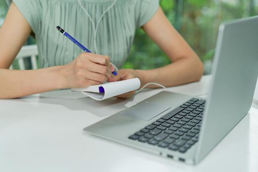 Happy businesswoman sitting and talking to colleagues in a meeting using her laptop computer and writing down notes