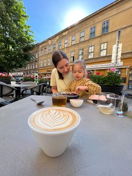 Cappuccino with a pattern on the foam stands on the table in front of the dining mother and daughter. High quality photo