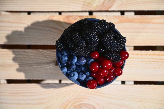 Flat lay. View from above of fresh and ripe organic wild berries from an organic farm- blueberries, blackberries and cherries in a ceramic bowl on wooden crate. Web banner, copy ad space for text
