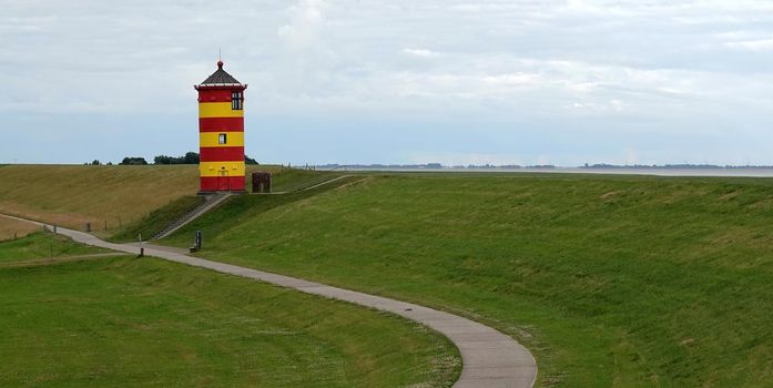 Cute German lighthouse in red and yellow. It's build in 1891 and 11 meters high. It's known as the Pilsum Lighthouse. It's standing on a dyke. Beneath the dyke is a bicycle road.
