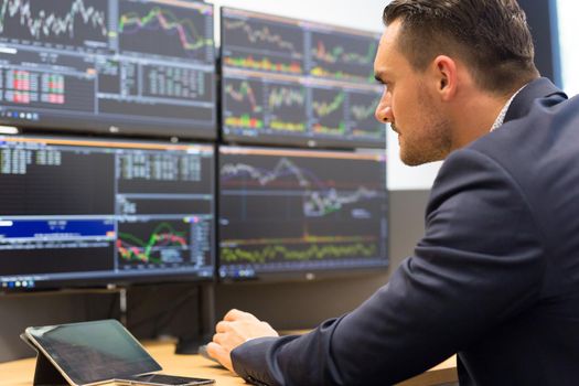 Stock broker trading online while accepting orders by phone. Trader's office with multiple computer screens full of index charts and data analyses.