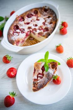Sweet cottage cheese casserole with strawberry filling, in a plate on a wooden table.