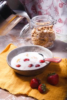 Summer breakfast with granola, fresh strawberry and milk pouring into plate, selective focus