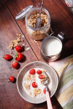 Summer breakfast with granola, fresh strawberry and milk on brown wooden table, flat lay