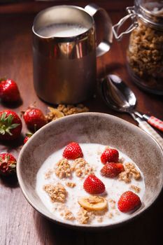 Summer breakfast with granola, fresh strawberry and milk on brown wooden table, selective focus