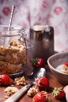 Homemade granola in glass jar with fresh strawberry and milk on brown wooden table, selective focus