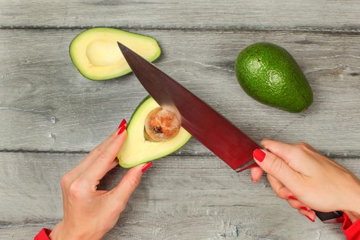 Table top view, woman removing avocado seed with chefs knife.