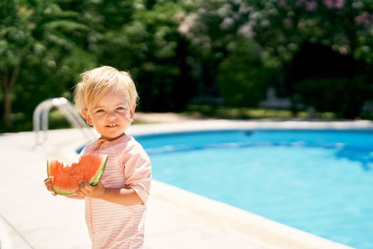 Little girl stands by the pool, holding a watermelon in her hands. High quality photo