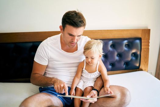 Dad reading a book to a little girl sitting on the bed. High quality photo