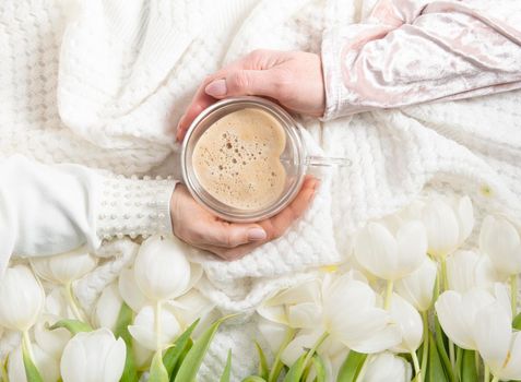 hands of two women holding a heart-shaped cup with cappuccino on two sides, female friendship, flat lay with white tulips, mother's day, valentine's day,