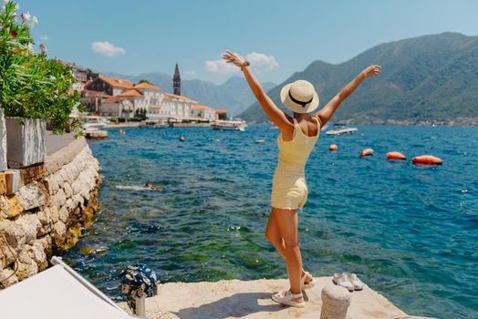 Summer photo shoot on the streets of Kotor, Montenegro. Beautiful girl in white dress and hat. smiling tourist girl with hat. Spectacular view of Montenegro with copy space. fashion outdoor photo of beautiful sensual woman with blond hair in elegant dress and straw hat and bag, posing in Montenego's city Perast