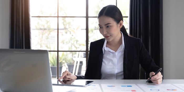 Portrait of Young Asian woman hand freelancer is working her job on computer tablet in modern office. Doing accounting analysis report real estate investment data, Financial and tax systems concept..