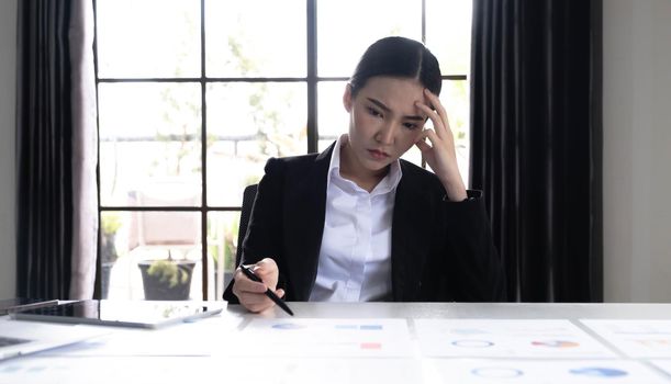 Image of an Asian woman who is tired and overthinking from working with a tablet at the office..