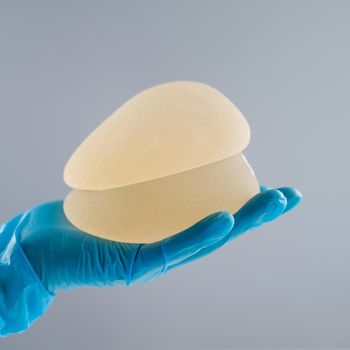 Doctor in a rubber glove holding a pile of breast implants