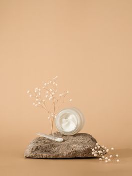 Cosmetic cream or moustirizer on stone over pastel beige background. Open round glass jar with aesthetic swirls face cream and spatula. Copy space. Vertical. Mockup