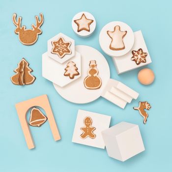 Christmas composition with gingerbread cookies in trendy minimalistic style. Different geometrical shapes, podiums and christmas cookies, flat lay or top view. Christmas baking on blue background