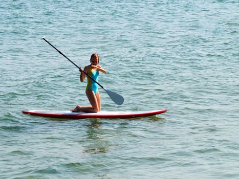 teenage girl riding a sup-board in the sea on her knees.