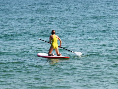 teenage girl riding a sup-board in the sea on her knees.