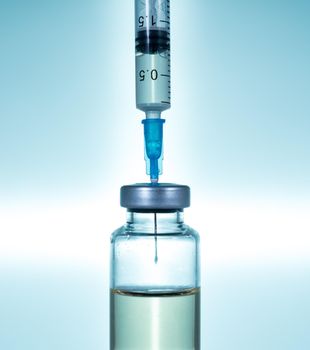 Macro of a hypodermic syringe or needle being filled with vaccine from bottle against a blue star background