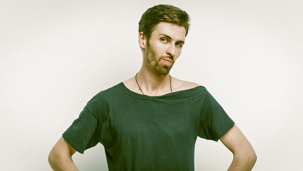 Strong Guy Looking Into The Camera While Standing Arms On His Hips, Stylish Fair-Skinned Bearded Man In A Black T-Shirt Posing On A Gray Background In The Studio