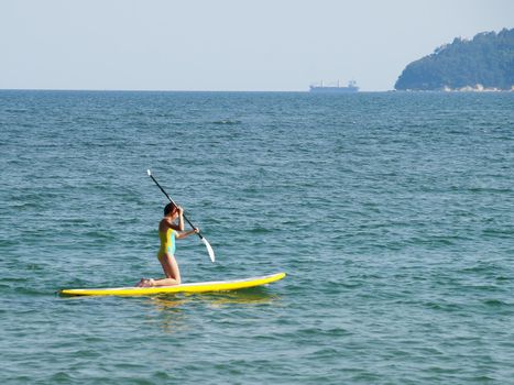 teenage girl riding a sup-board in the sea on her knees.